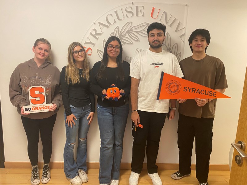 Students smiling and holding Syracuse University items banner
				